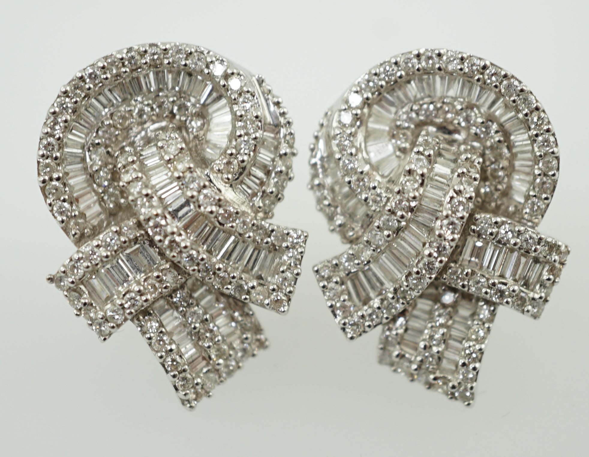 A pair of 18k white gold and pave set round and baguette cut diamond cluster set 'knot' earrings
